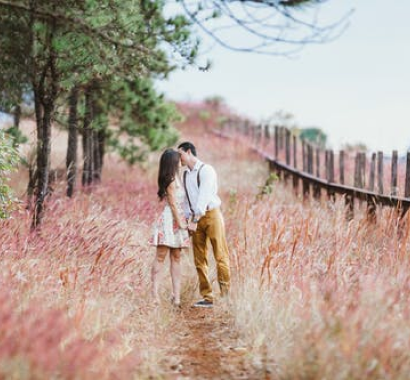 A couple walking down a path surrounded by trees and tall grass